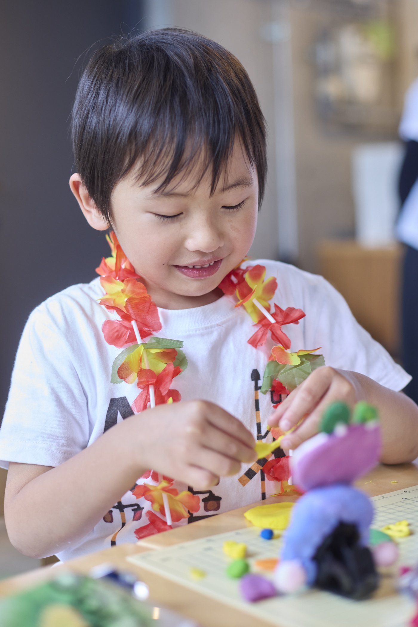 花のレイをつけてカラフルなねんどのキャラクターを作る男の子